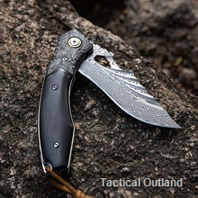 VG10 Damascus folding knife resting on textured outdoor rock