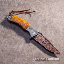Coreless Damascus folding knife with orange wood-grain handle outdoors
