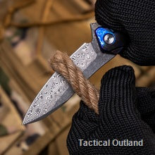 Damascus folding knife held in a gloved hand outdoors
