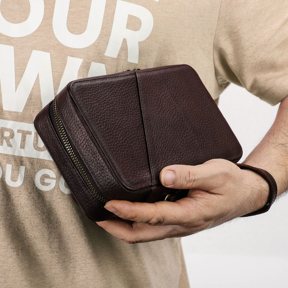 Hand carrying the compact brown leather tech organizer by its wrist strap