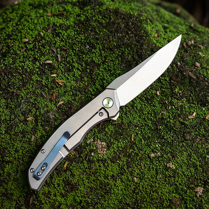 M390 outdoor folding utility knife on a mossy field background